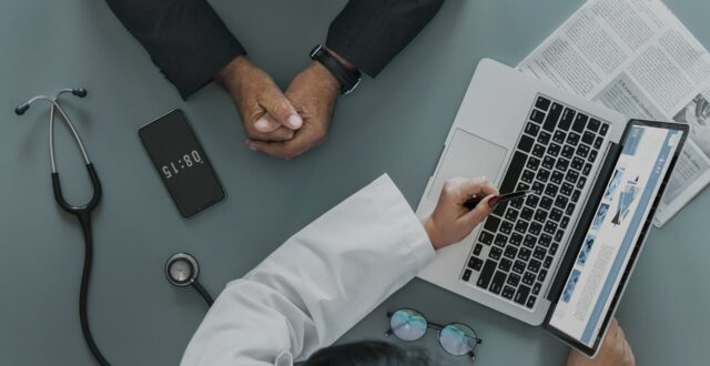 overhead shot of physician explaining insurance options to a male patient on a laptop